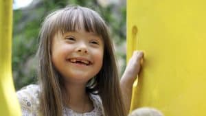 Bright smiling young girl enjoying outdoor play on yellow playground equipment, showcasing happiness and child development in a safe environment.