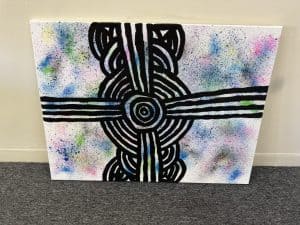 Abstract artwork featuring a black labyrinth-like design on a colorful, splattered background, displayed on a white wall, symbolizing creativity and modern interior decor