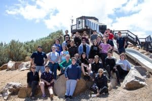 Friendly group of young people and staff enjoying a sunny day at an outdoor adventure park, engaging in team-building activities as part of inclusive recreational programs supported by Assured Care Solutions.